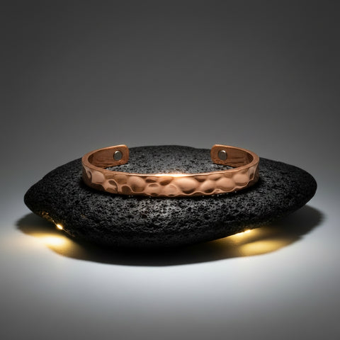 A hammered copper cuff bracelet displayed on a dark textured stone against a dark gray gradient background.