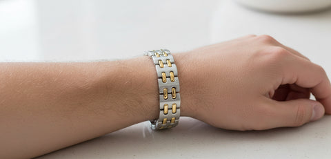 Hand wearing a silver and gold bracelet on a light background