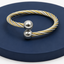 Bracelet with gold and silver cables on a dark blue circular stand