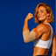 A woman with blonde hair flexes her bicep against a solid blue background, wearing a white sports bra, black leggings, and a beige elbow sleeve.