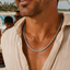 A close-up lifestyle shot of a man wearing Golfers All Silver B-NL,  a silver-toned chain necklace with a black and silver patterned link design, styled with a light beige linen shirt on a sunny beach boat deck.