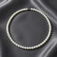 Pearl necklace with a silver-toned clasp, arranged in a circle on a dark gray satin fabric background.
