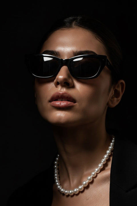 A close-up portrait of a woman a white  pearl magnetic necklace against a dark black background.